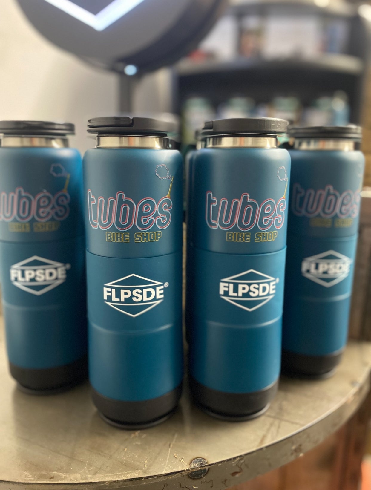 Four blue insulated drink containers with 'tubes' and 'FLPSDE' branding on a wooden surface.